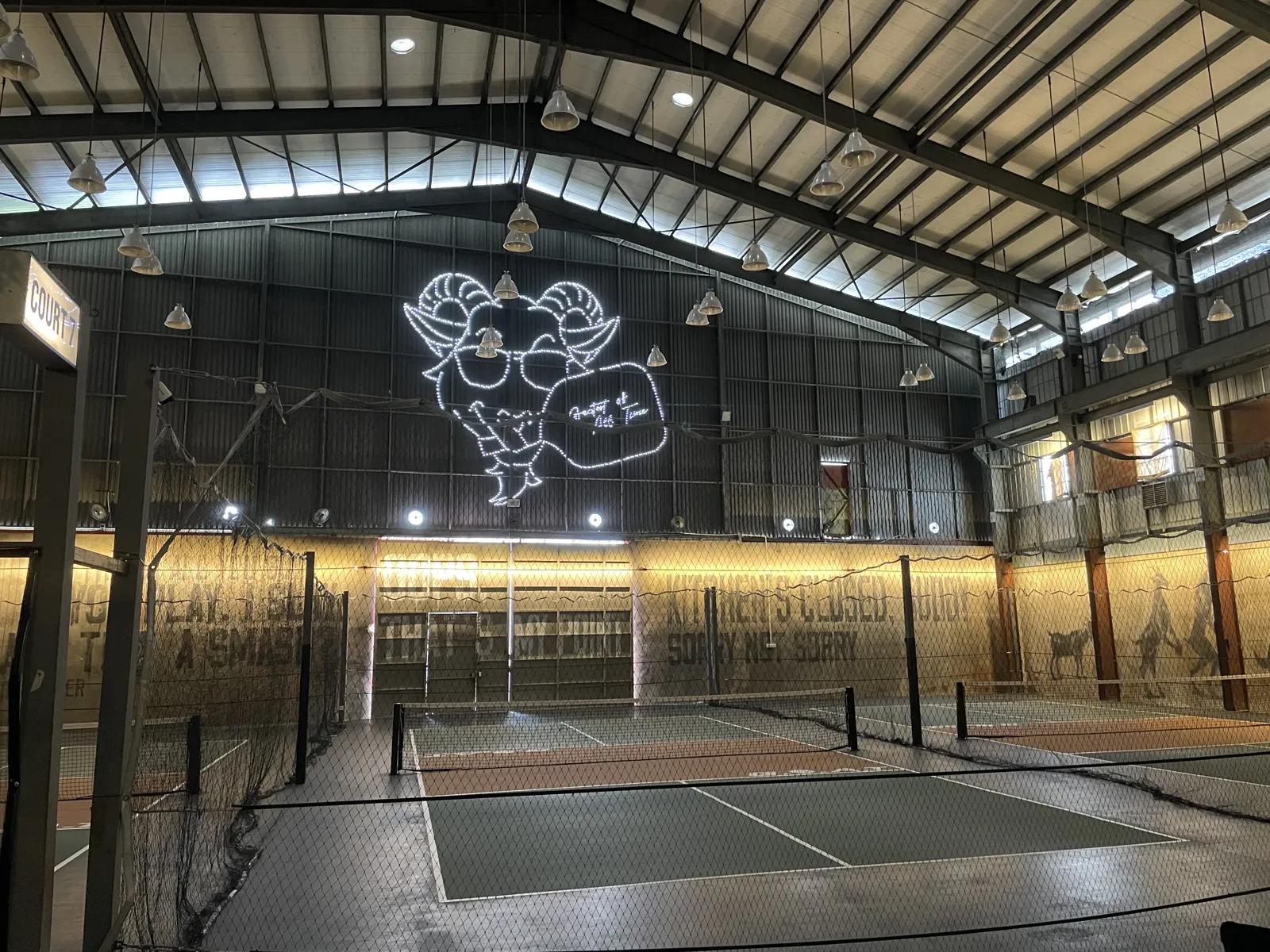 The neon goat logo on the wall above the courts at G.O.A.T Pickle Club III